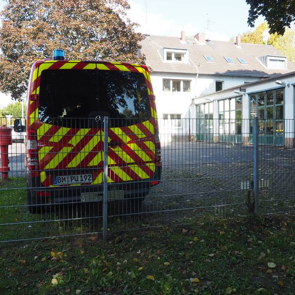 Links vorne ein Einsatzfahrzeug vor einem Feuerwehrgerätehaus.