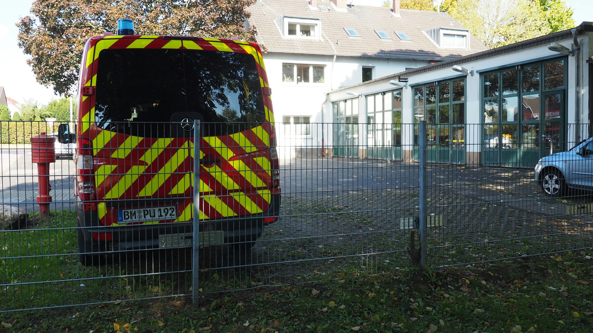 Links vorne ein Einsatzfahrzeug vor einem Feuerwehrgerätehaus.