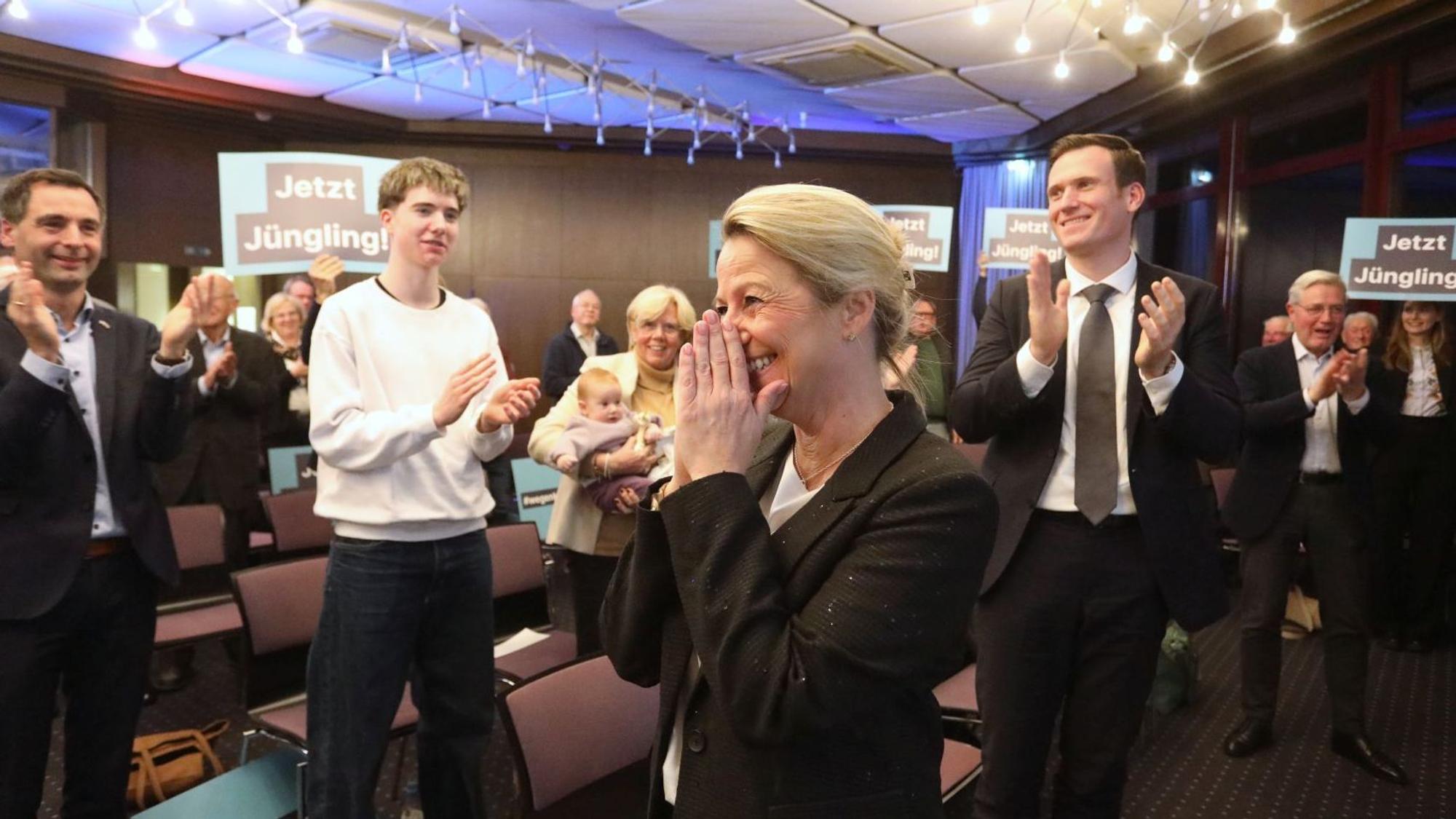 Mehrere Menschen applaudieren einer Frau, teilweise halten sie Schilder mit der Aufschrift „Jetzt Jüngling“ in die Höhe.