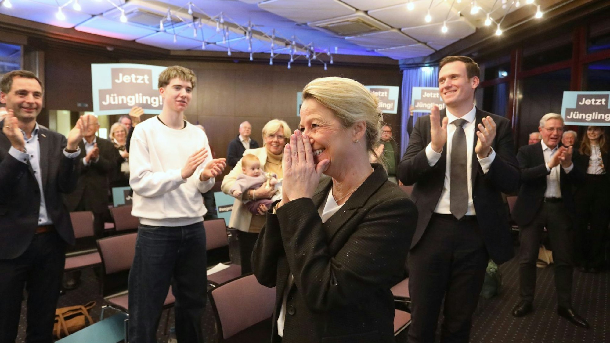 Mehrere Menschen applaudieren einer Frau, teilweise halten sie Schilder mit der Aufschrift „Jetzt Jüngling“ in die Höhe.