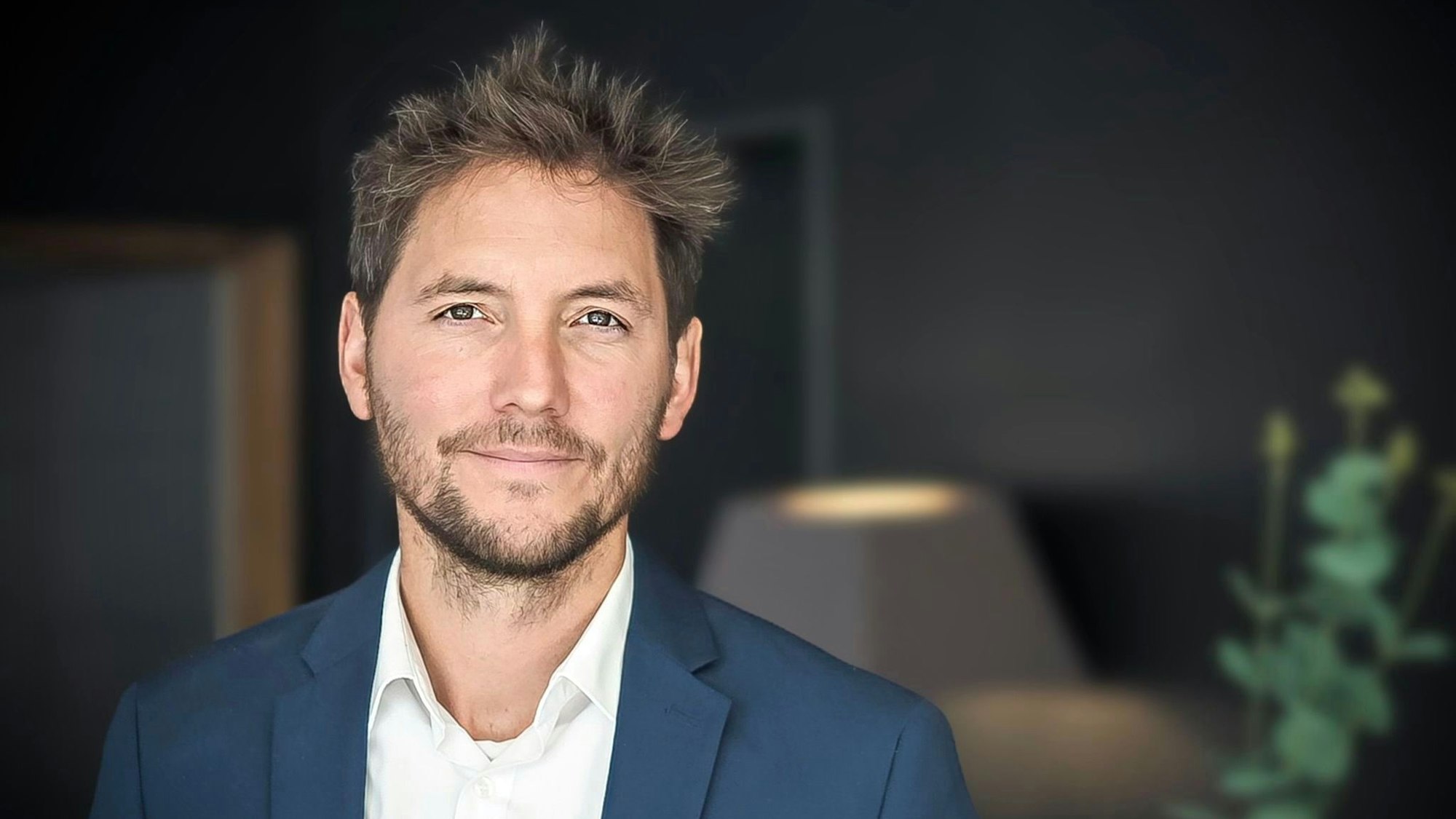 Porträt von Dirk Weiermann. Er trägt ein offenes weißes Hemd, ein blaues Sakko und einen Dreitagebart.