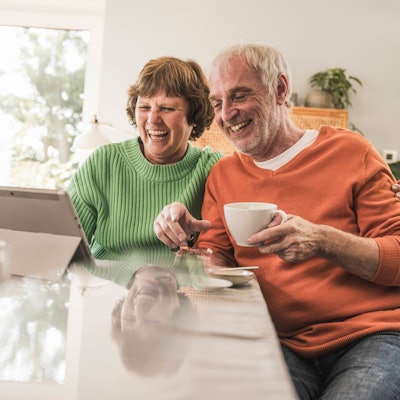 Eine ältere Frau und ein älterer Mann sitzen lachend an einem Tisch vor einem Tablet