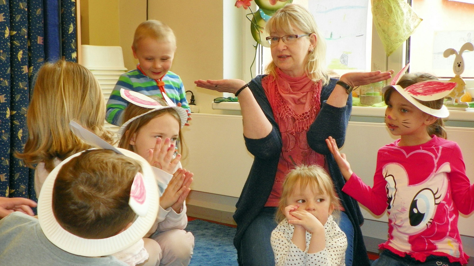 Eine Frau und Kinder sitzen zusammen auf einem Teppich. Die Kinder tragen selbstgemachte Hasenohren.
