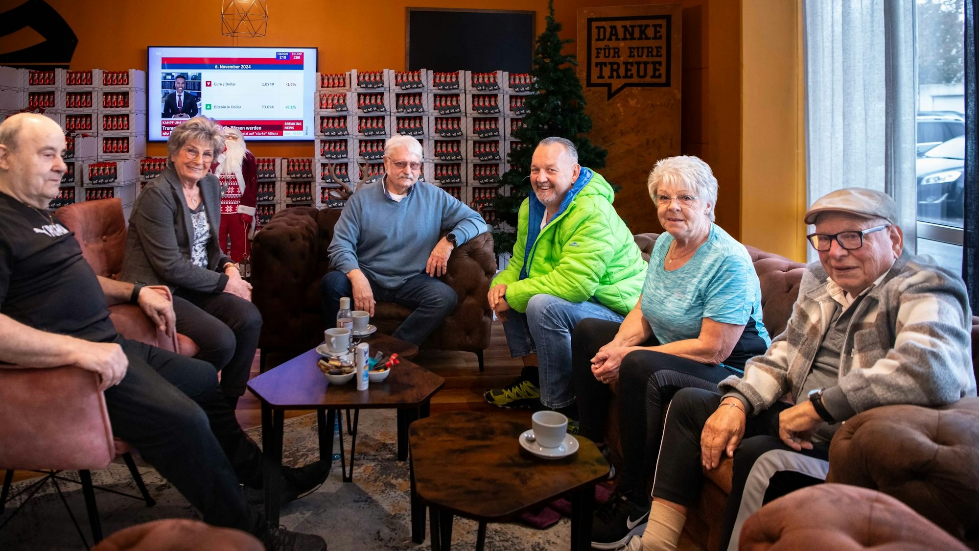 Das Bild zeigt sechs Senioren auf Sesseln und einer Couch im Fitnessstudio sitzen.