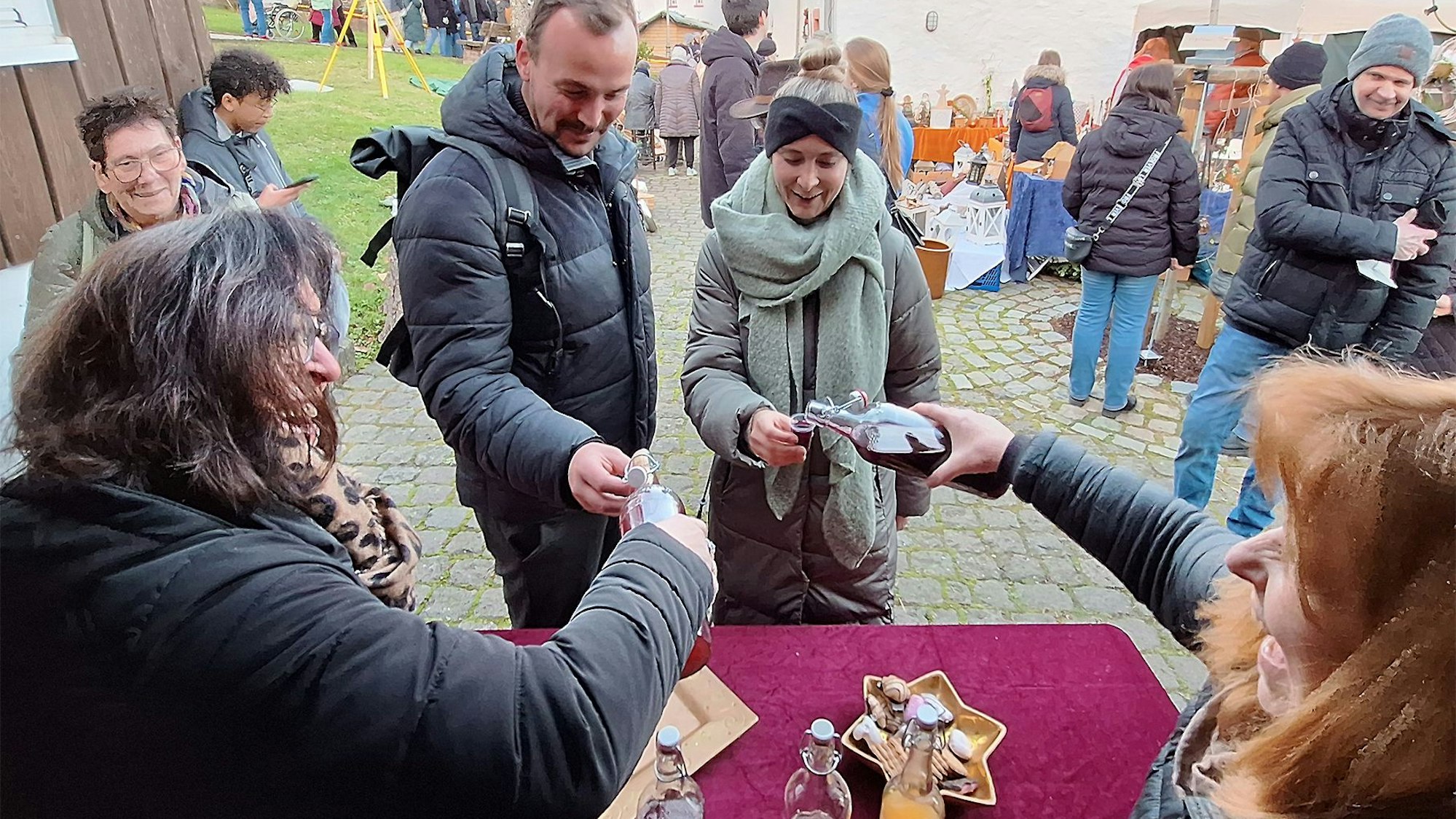 Das Bild zeigt Carmen und Elke Huppertz, die Gästen vor ihrem Stand einen Likör einschenken.