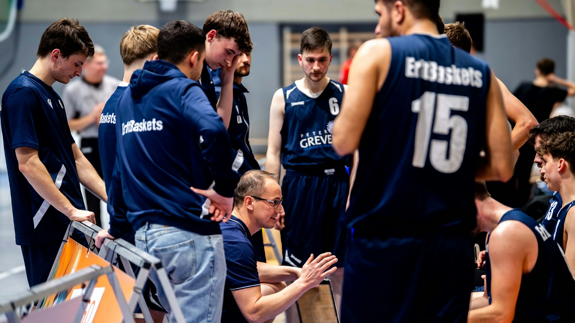 Der Trainer kniet gestikulierend auf dem Boden, umgeben von Spielern, die ihm zuhören.