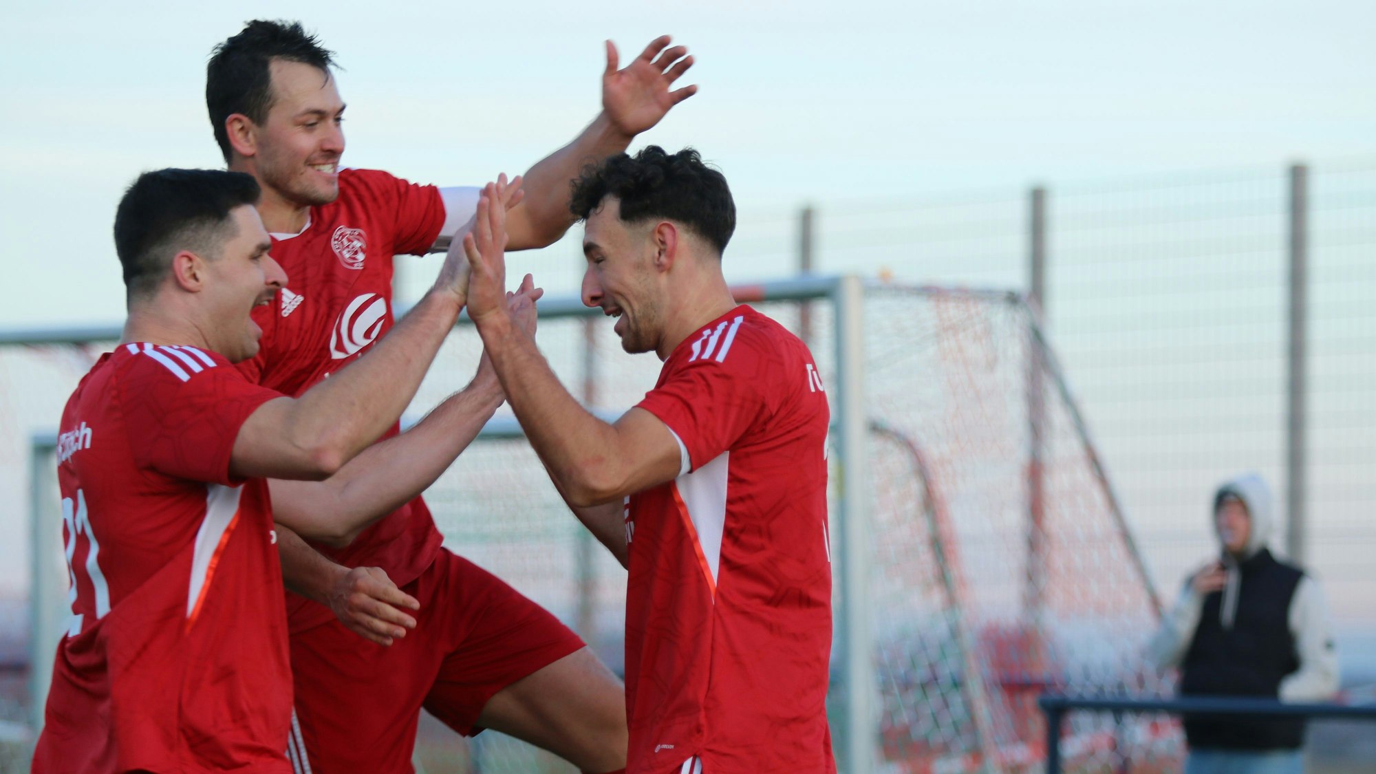 Drei Fußballer jubeln und klatschen einander ab.