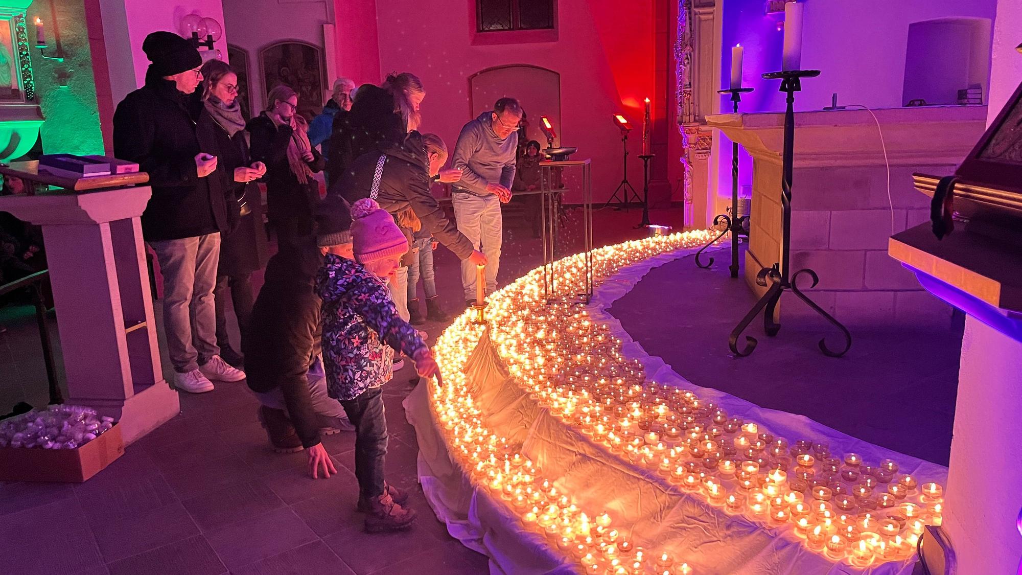 Menschen in einer bunt beleuchteten Kirche. Auf den Stufen leuchten Lichterkette.