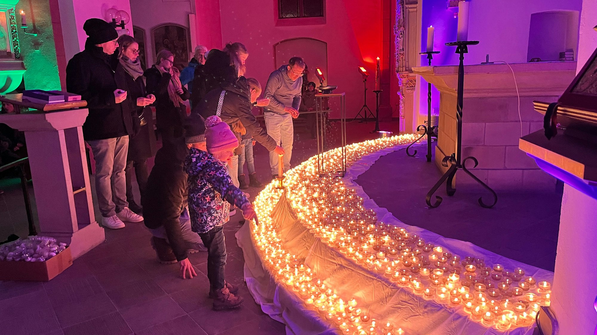 Menschen in einer bunt beleuchteten Kirche. Auf den Stufen leuchten Lichterkette.