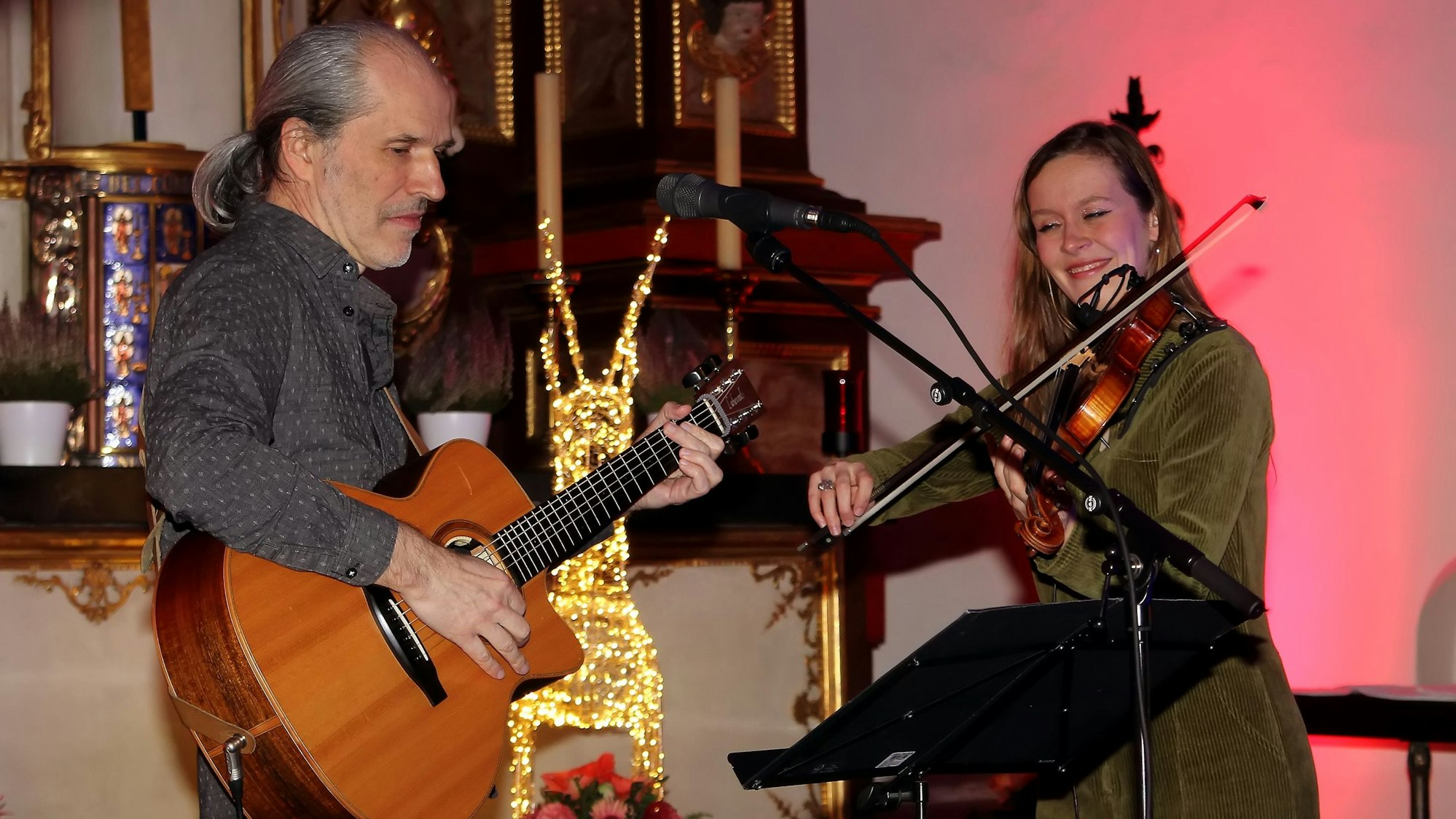Peter Schneider spielt Gitarre, Jördis Thielsch Geige. Die beiden stehen nebeneinader in der Kirche St. Alban.