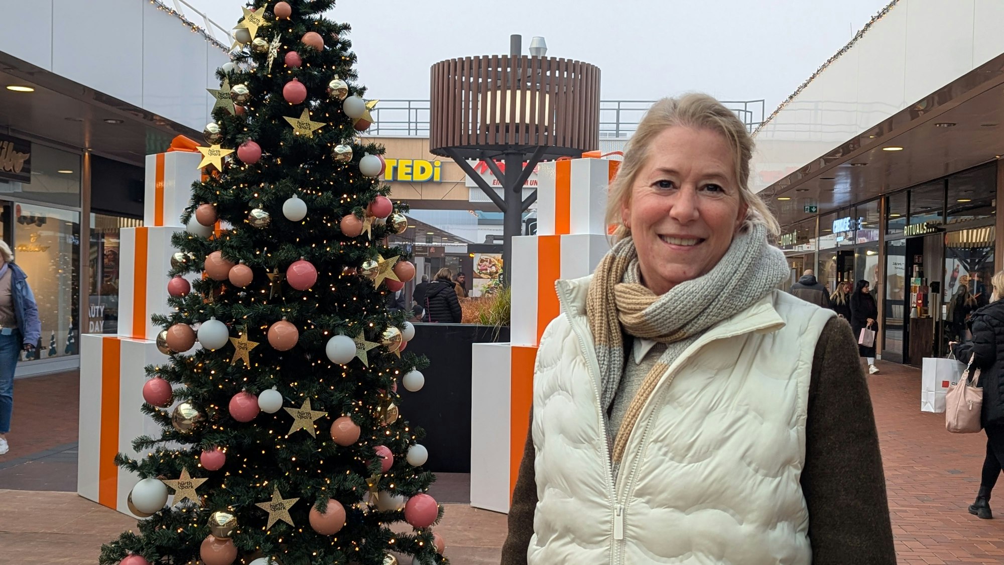 Das Foto zeigt die Center-Managerin neben einem großen Weihnachtsbaum in einer Einkaufspassage im Hürth-Park.