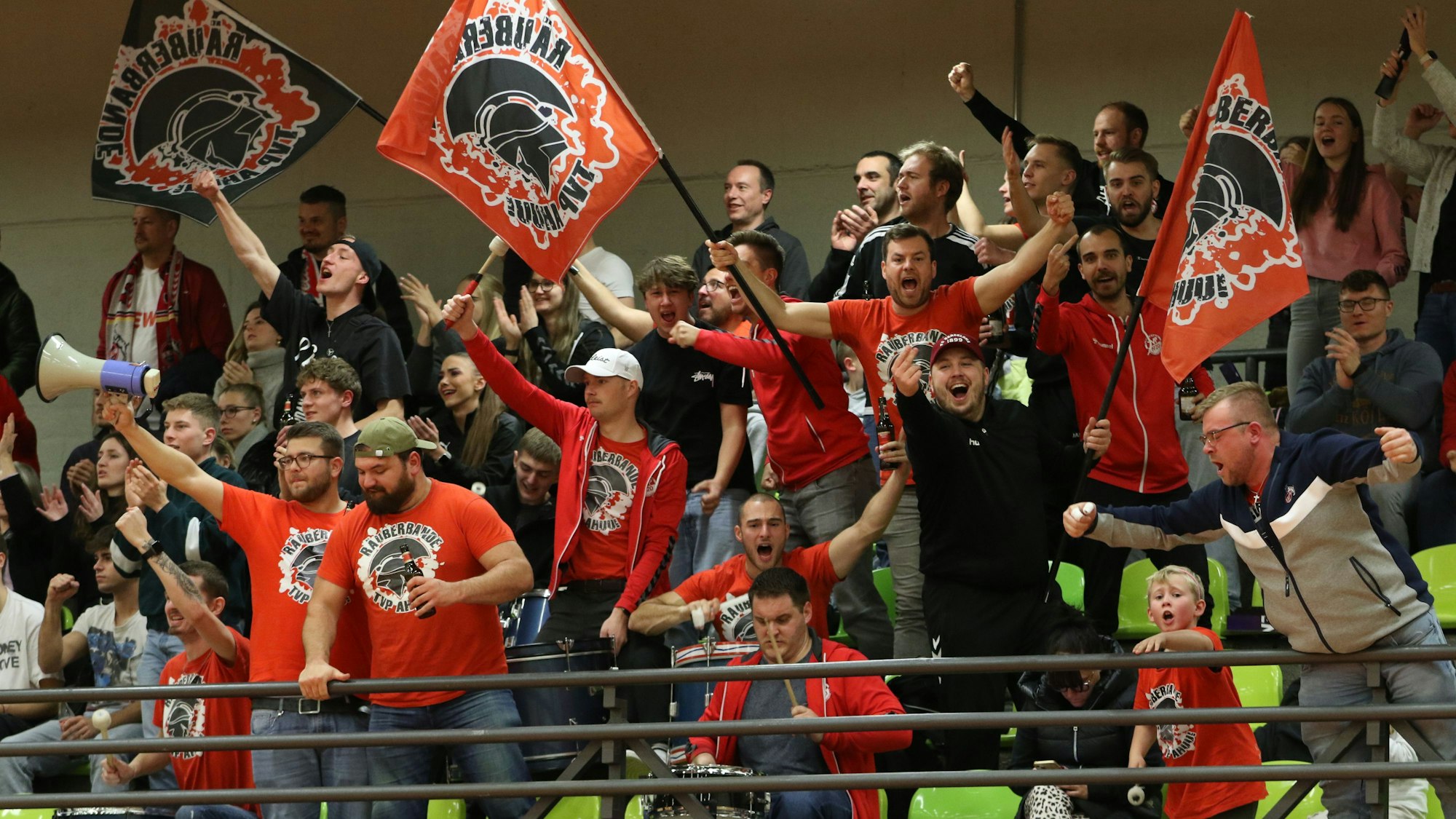 Auf der Tribüne jubeln die Fans, einige schwenken Fahnen.