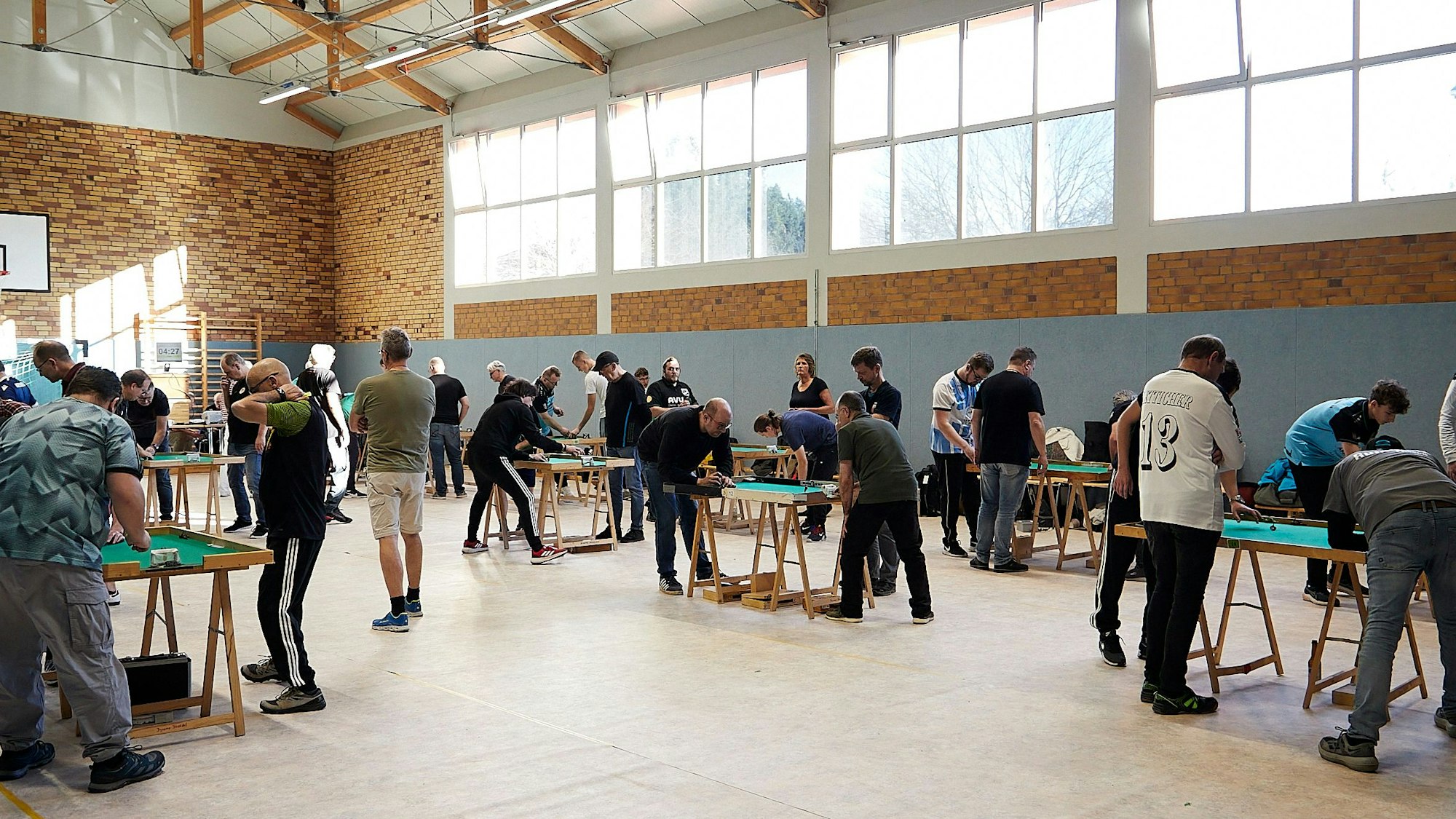 Sieben der 12 Tische sind auf dem Foto zu sehen. Um jeden Tisch stehen mehrere Spieler und Schiedsrichter.