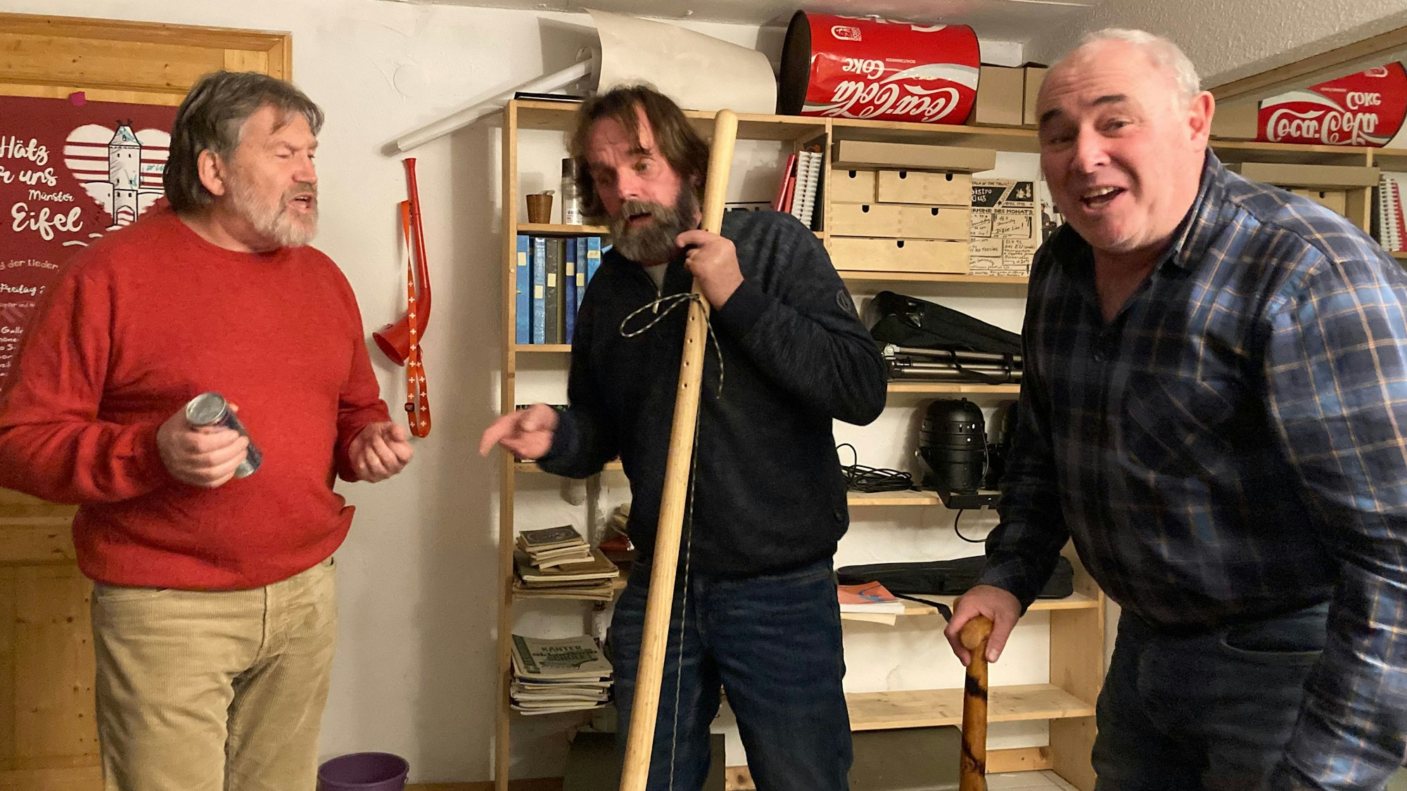 Drei ältere Herren stehen in einem Keller und singen. Sie halten provisorische Instrumente.