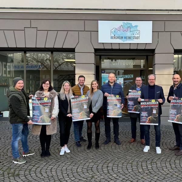 Zu sehen sind verschiedene Akteure aus Stadt und Kultur, die Plakate für das Nikolaussingen hochhalten.