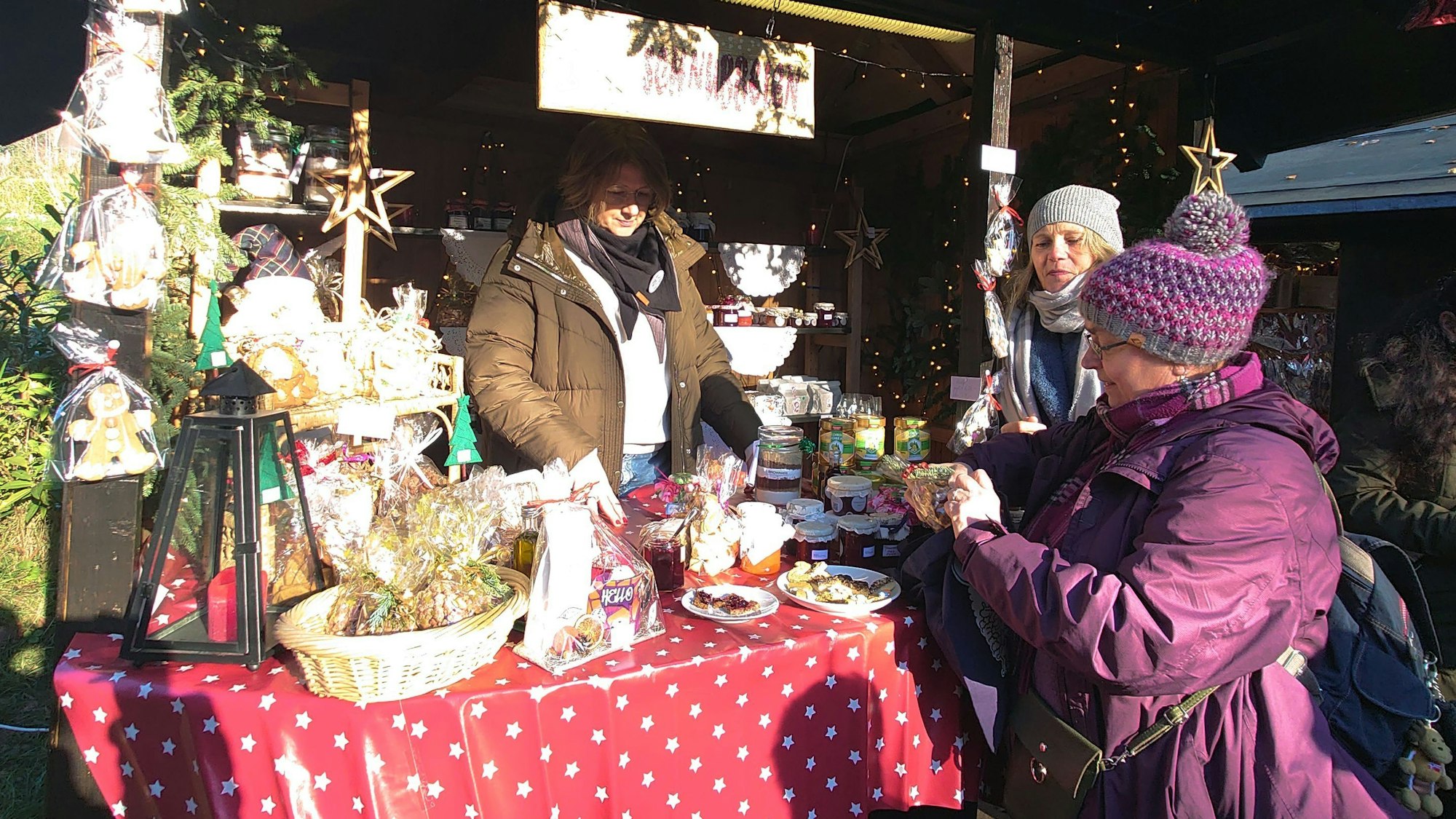 Eine Frau verkauft Gläser an zwei Frauen vor ihrem Stand.