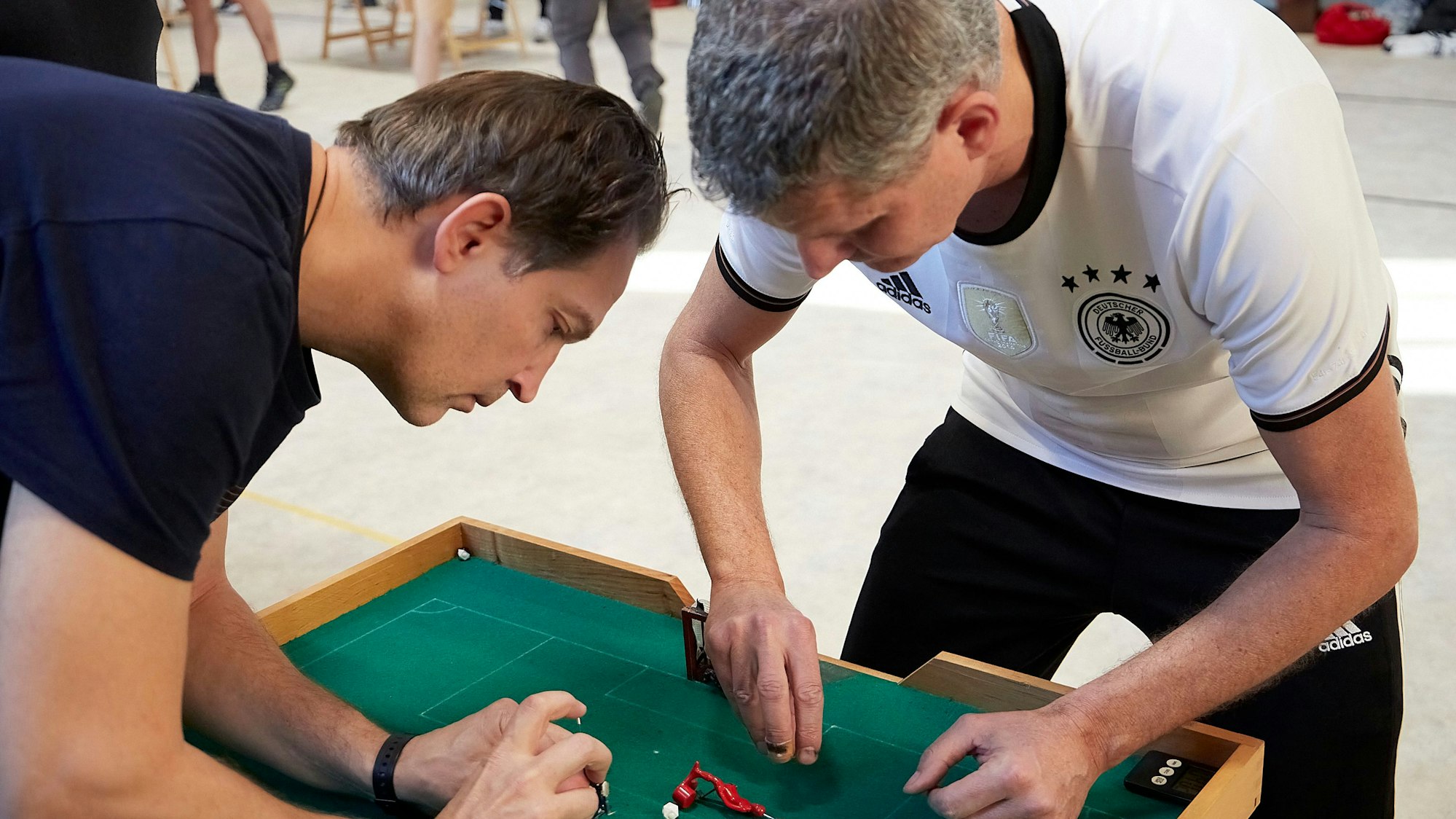 Artur Merke und Frank Hampel beugen sich über den Tisch und bewegen ihre Spieler-Figürchen.