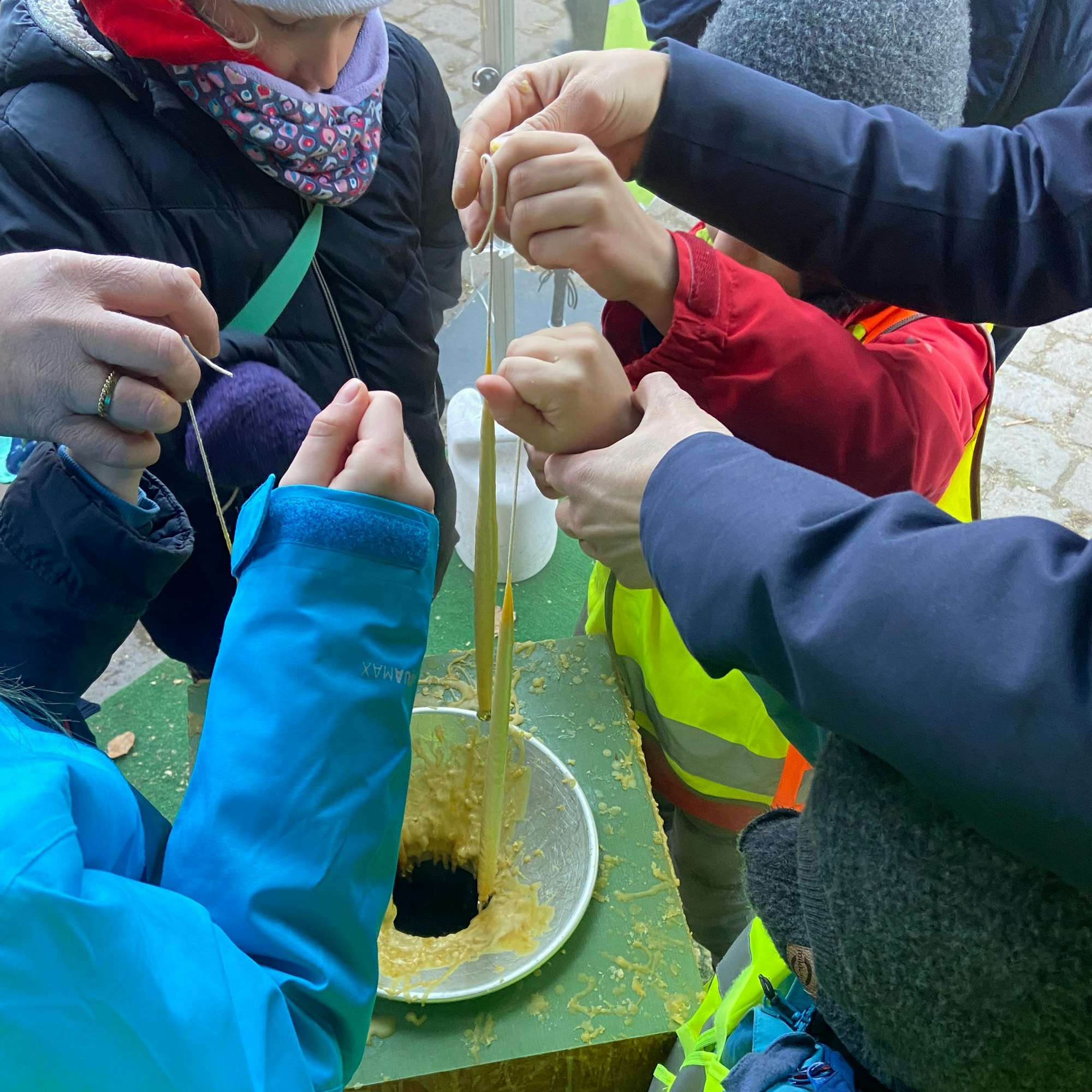 Kinder ziehen Kerzen aus einem Behältnis mit flüssigem Wachs.