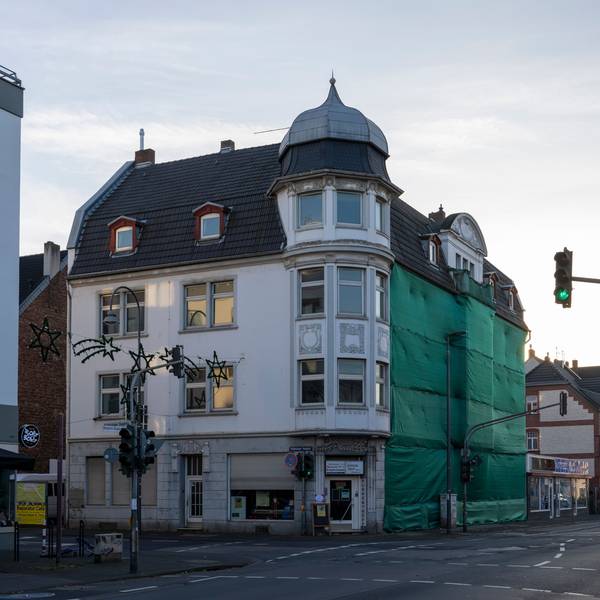 Blick auf ein Eckhaus, dessen Fassade zum Teil verhängt ist.
