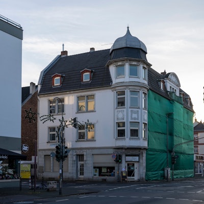Blick auf ein Eckhaus, dessen Fassade zum Teil verhängt ist.