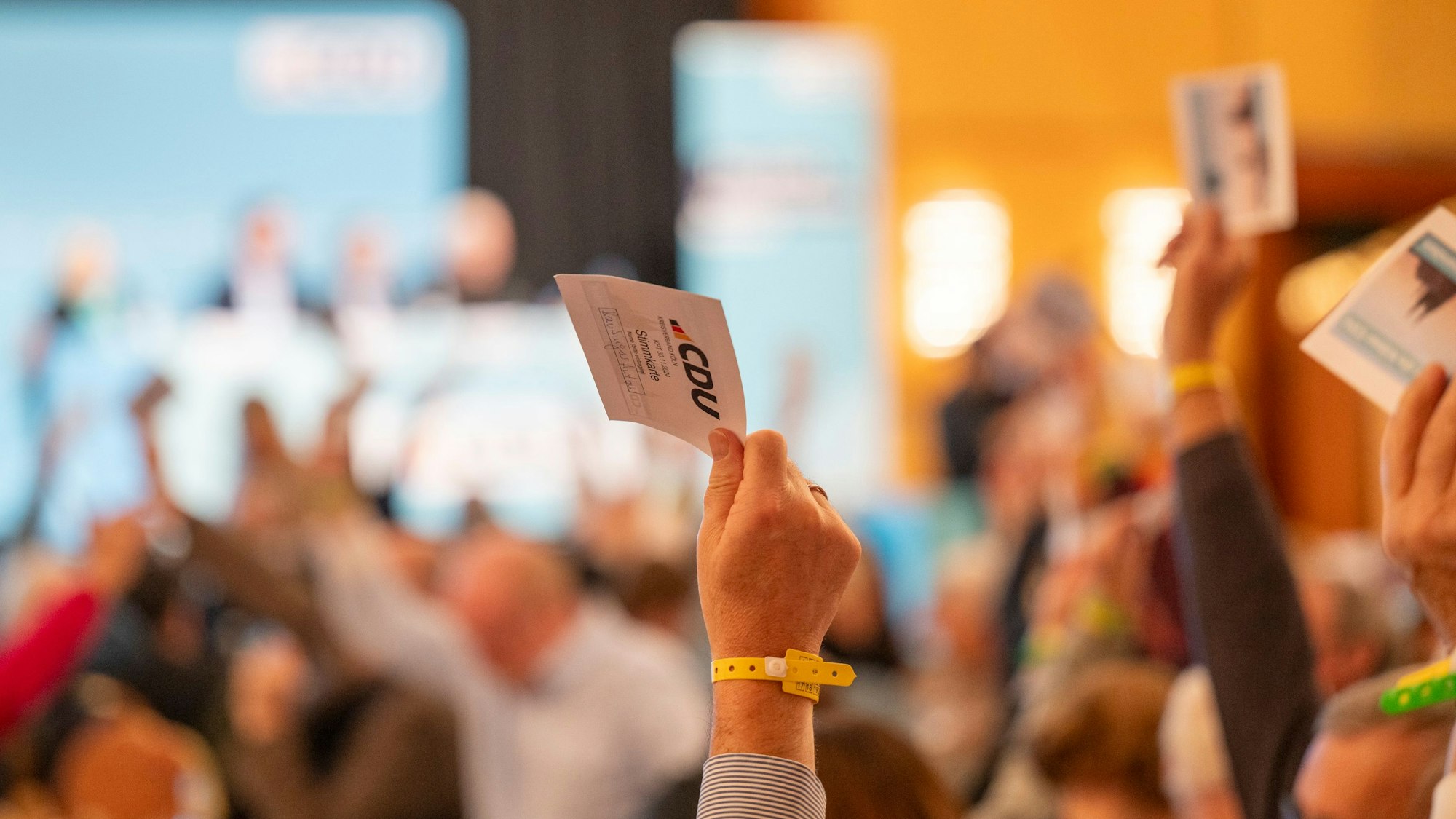 Das Bild zeigt ein Saal mit Personen, die gerad per Hand abstimmen.