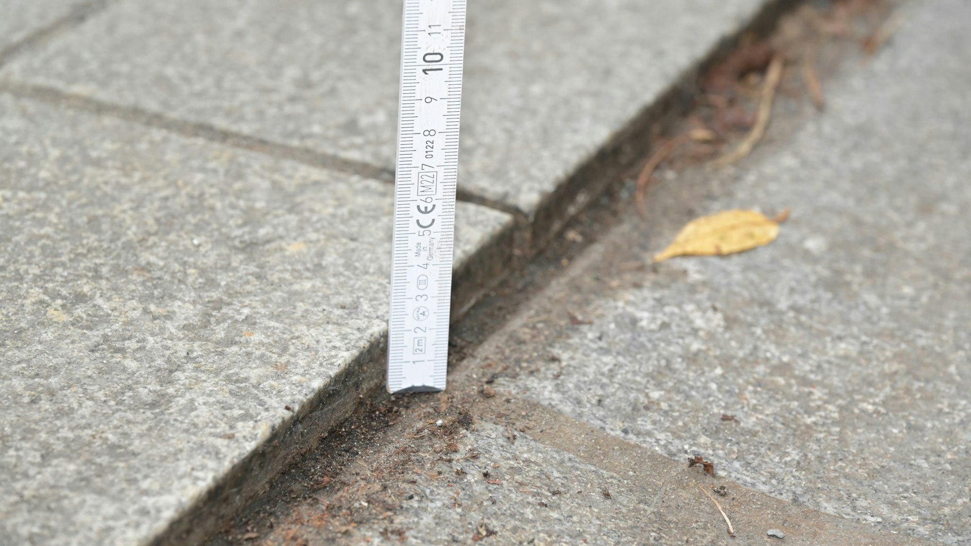 Ein Zollstock zeigt einen Höhenunterschied von zwei Zentimetern zwischen Regenrinne und Bodenbelag.