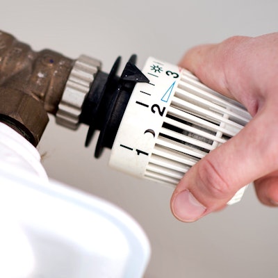 Eine Hand dreht am Thermostat eines Heizkörpers. (Symbolbild)