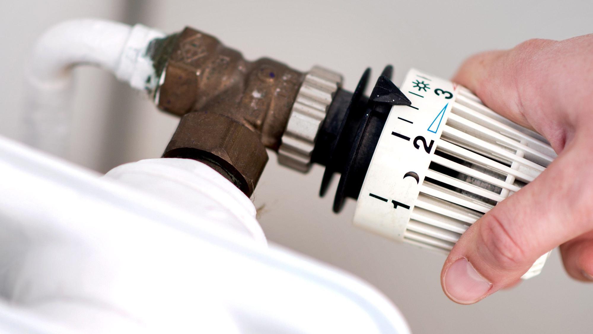 Eine Hand dreht am Thermostat eines Heizkörpers. (Symbolbild)