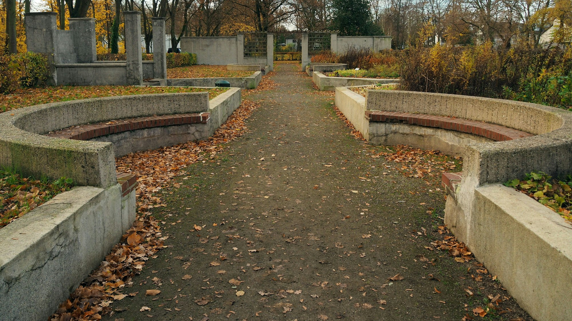 Blick auf einen breiten Parkweg, der halbkreisförmige Sitznischen bietet