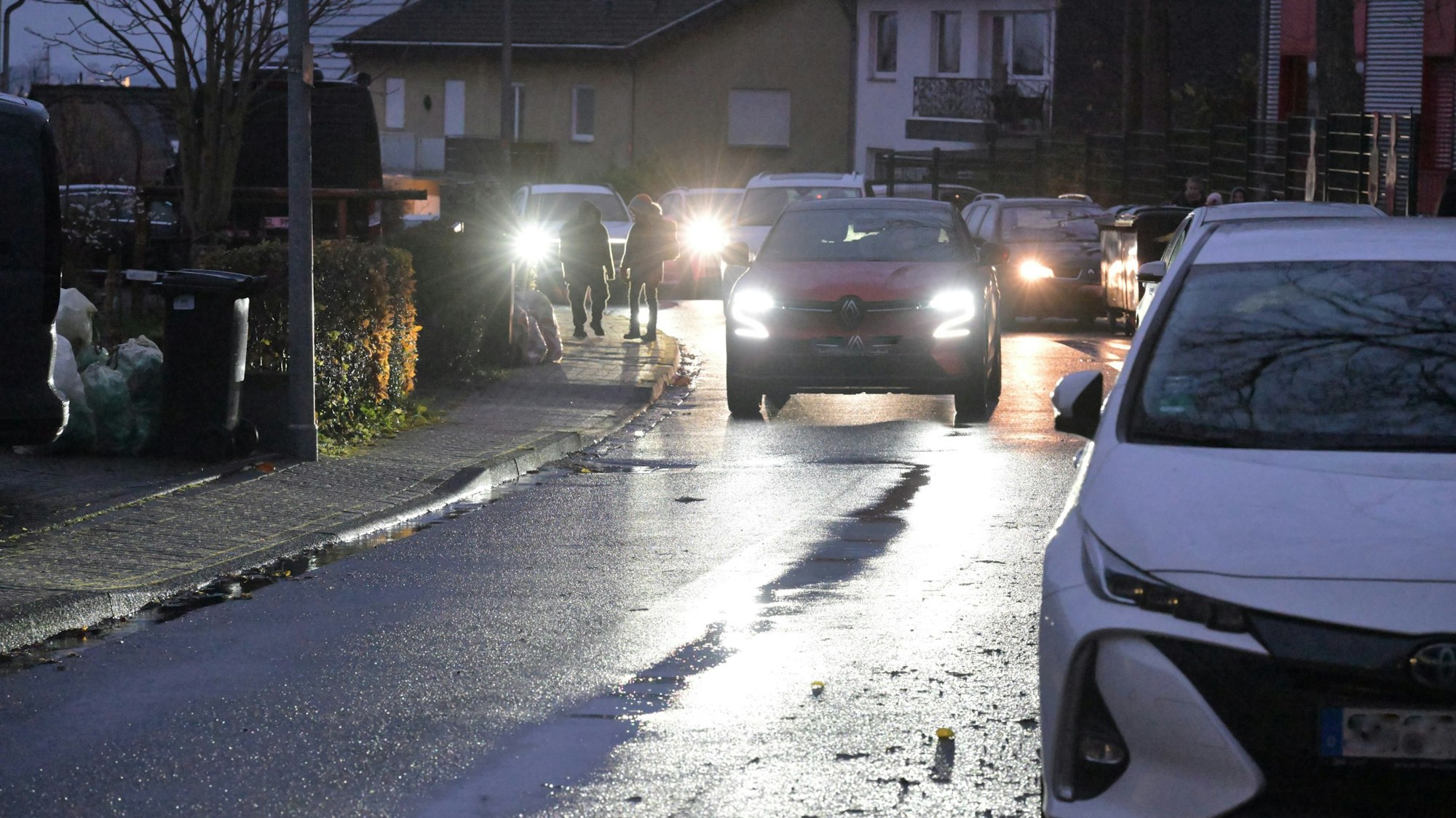 Auf der schmalen Straße parken Autos und verengen die Fahrbahn.