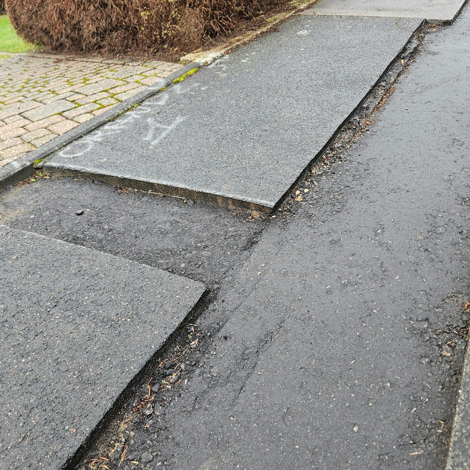 Zu sehen ist ein Bürgersteig mit scharfen Kanten an den Stellen, an denen Asphalt fehlt.