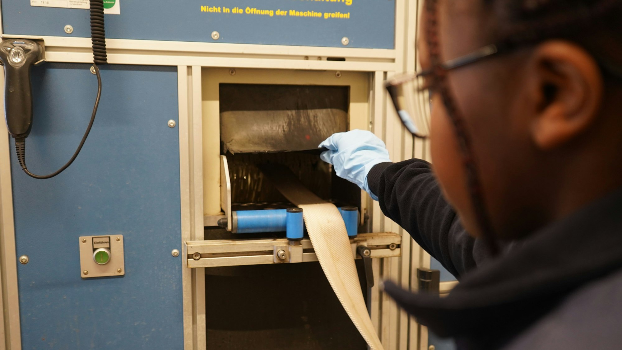 Das Foto zeigt eine junge Frau, die einen Feuerwehrschlauch in einer Maschinen-Öffnung kontrolliert.