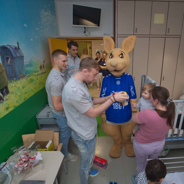 Drei Handballer überreichen in einem Krankenzimmer einem kleinen Jungen ein Spielzeug.
