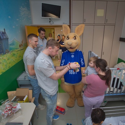Drei Handballer überreichen in einem Krankenzimmer einem kleinen Jungen ein Spielzeug.