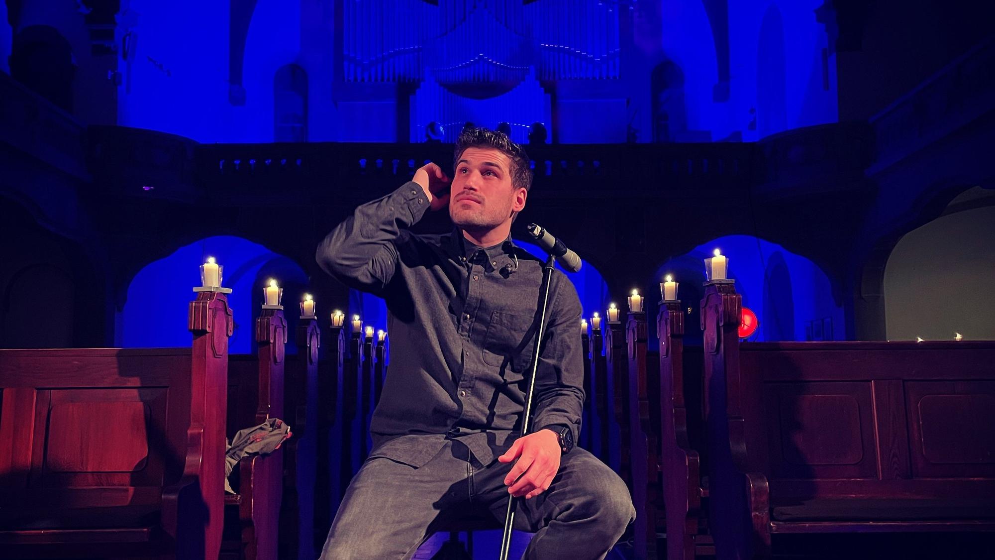 Dominic Sanz posiert in der Mannheimer Friedenskirche auf einem Stuhl hinter einem Mikrofon und schaut in die Ferne.
