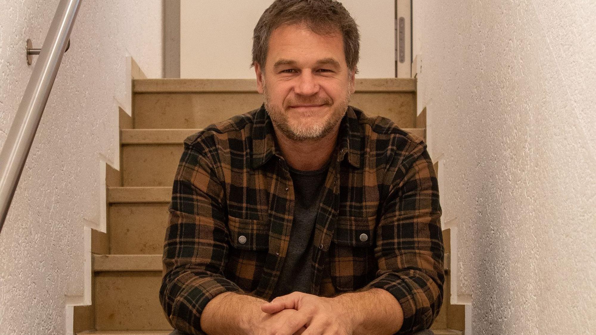Christian Golz sitzt auf einer Treppenstufe und lächelt in die Kamera.