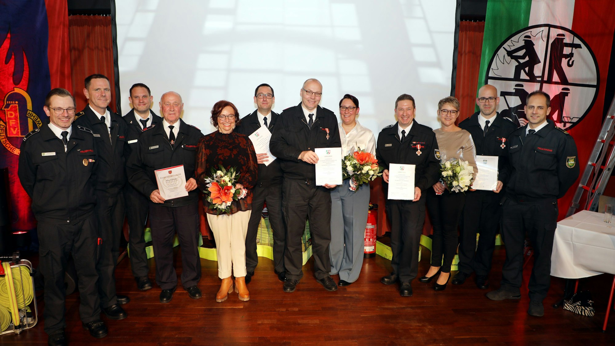 Jubilare und Ausgezeichnete stehen mit Einheitsführern und Wehrleitung auf der Bühne im Spiegelsaal des Bergischen Löwen.