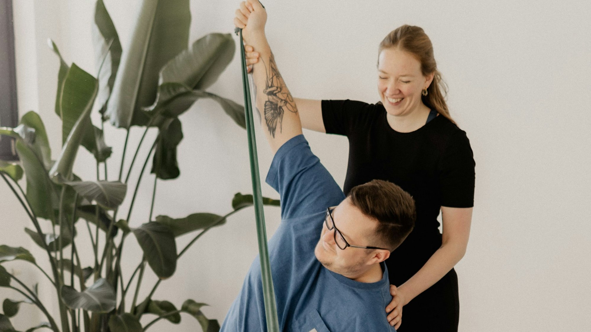 Das Bild zeigt eine Yoga-Lehrerin, die mit einem Mann eine Übung im Sitzen durchführt.