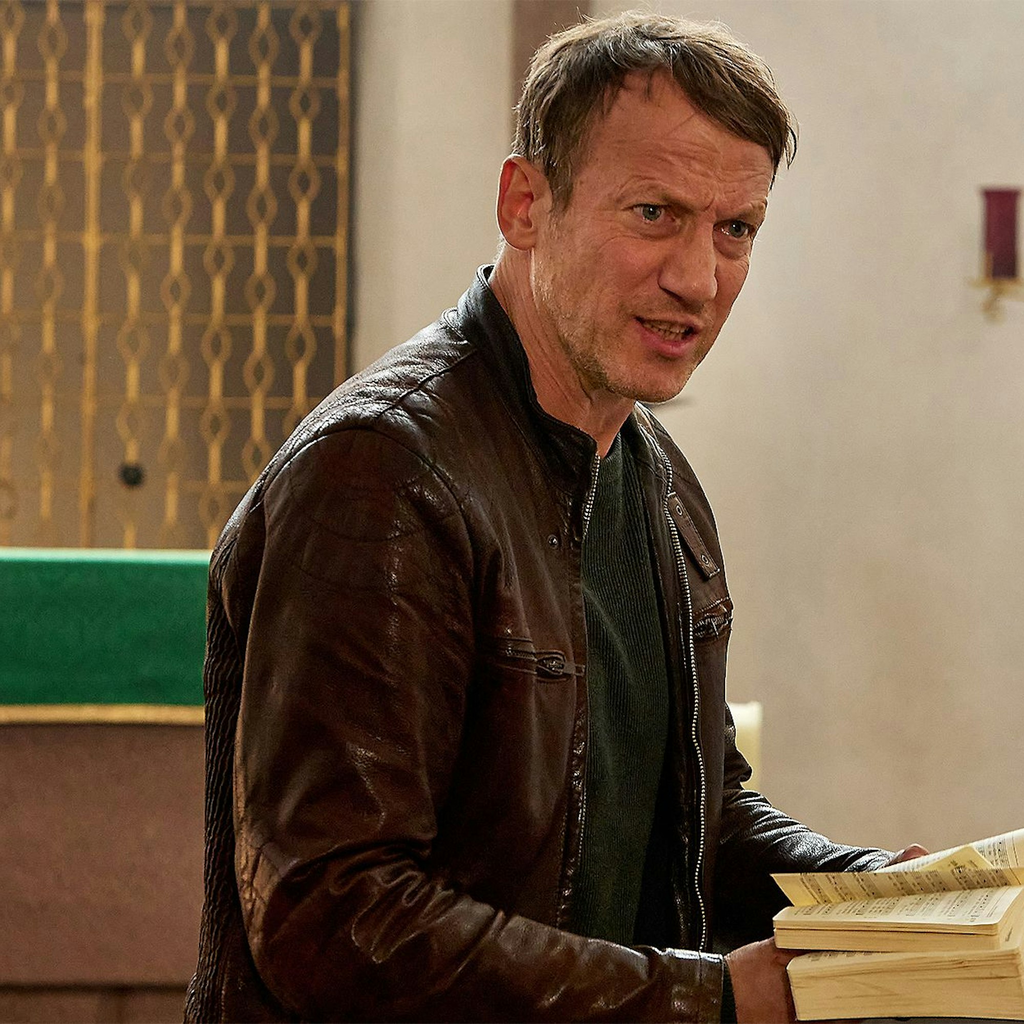 Szenenfoto mit Wotan Wilke Möhring, der in einem Gesangsbuch blättert.