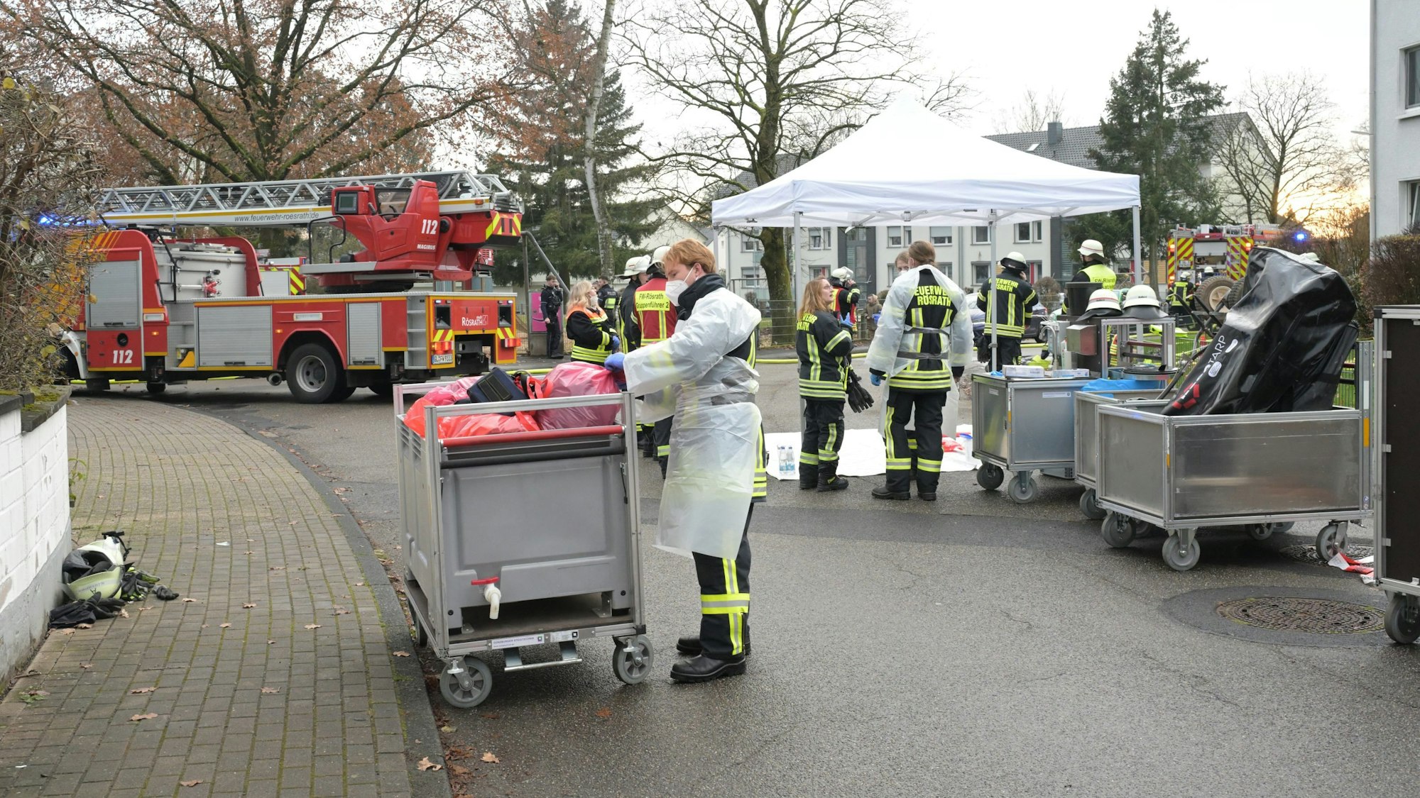 Menschen in Kitteln stehen an einem Pavillon und einem Rollwagen.