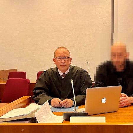 Zwei Männer an einem Tisch, auf dem ein Laptop steht.