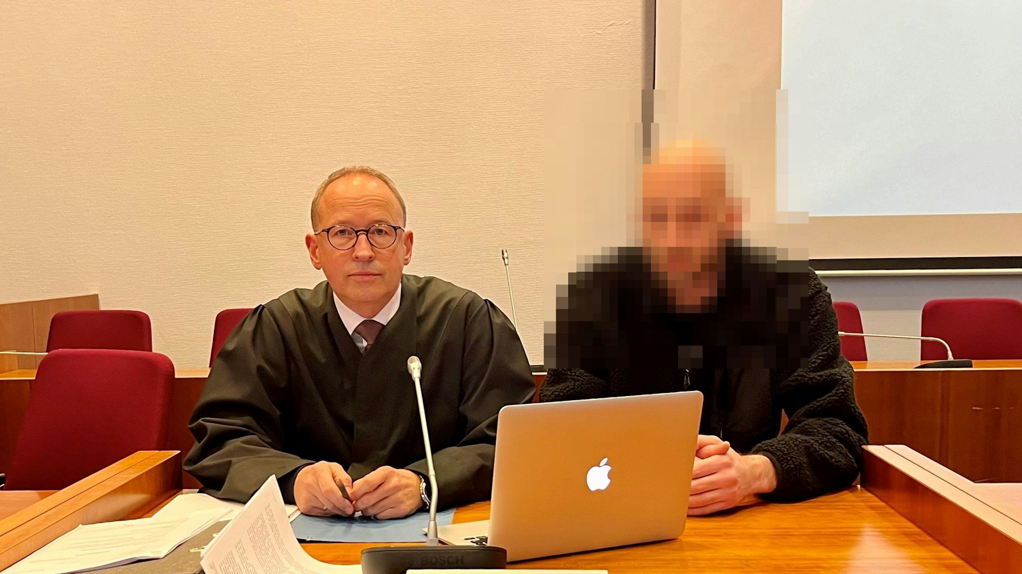 Zwei Männer an einem Tisch, auf dem ein Laptop steht.