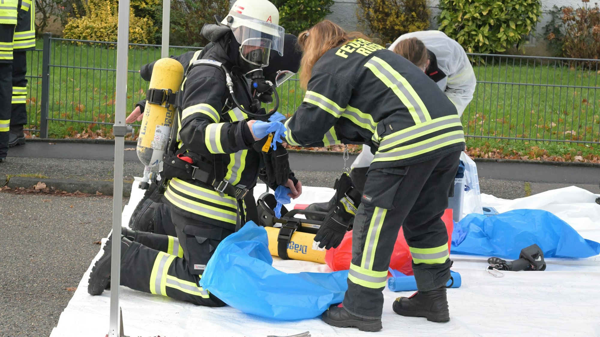 Feuerwehrleute ziehen Kleidung aus und packen sie in blaue Säcke.