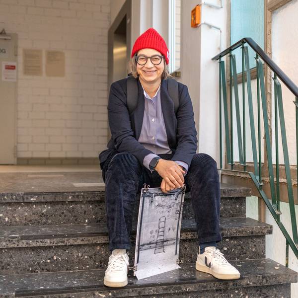 Claudia Mewaldt sitzt mit einem ihrer Bilder auf einer Treppe im Treppenhaus.