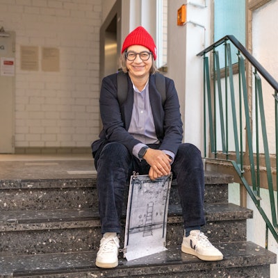 Claudia Mewaldt sitzt mit einem ihrer Bilder auf einer Treppe  im Treppenhaus.