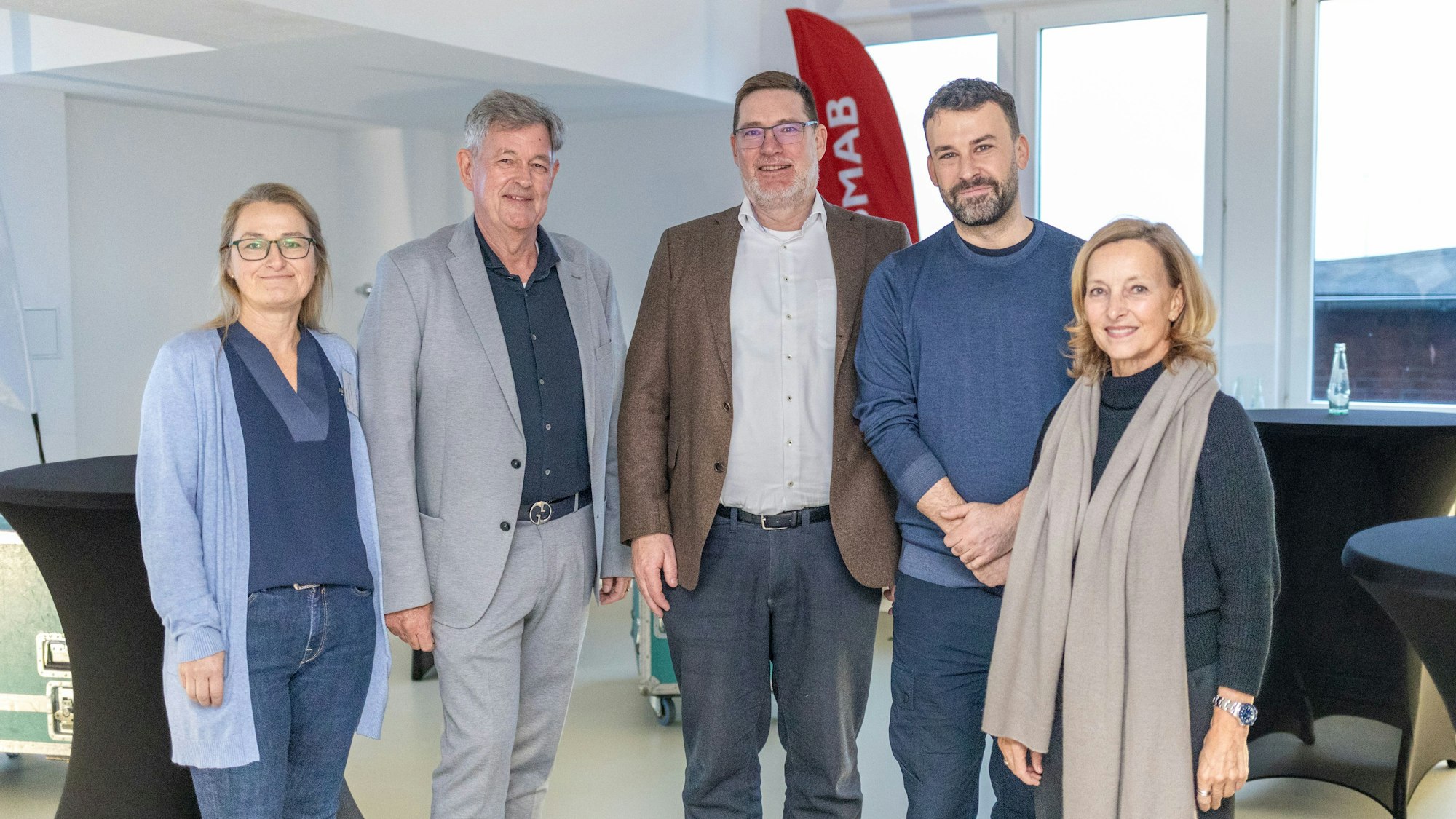 Fünf Menschen stehen nebeneinander in einem Raum.