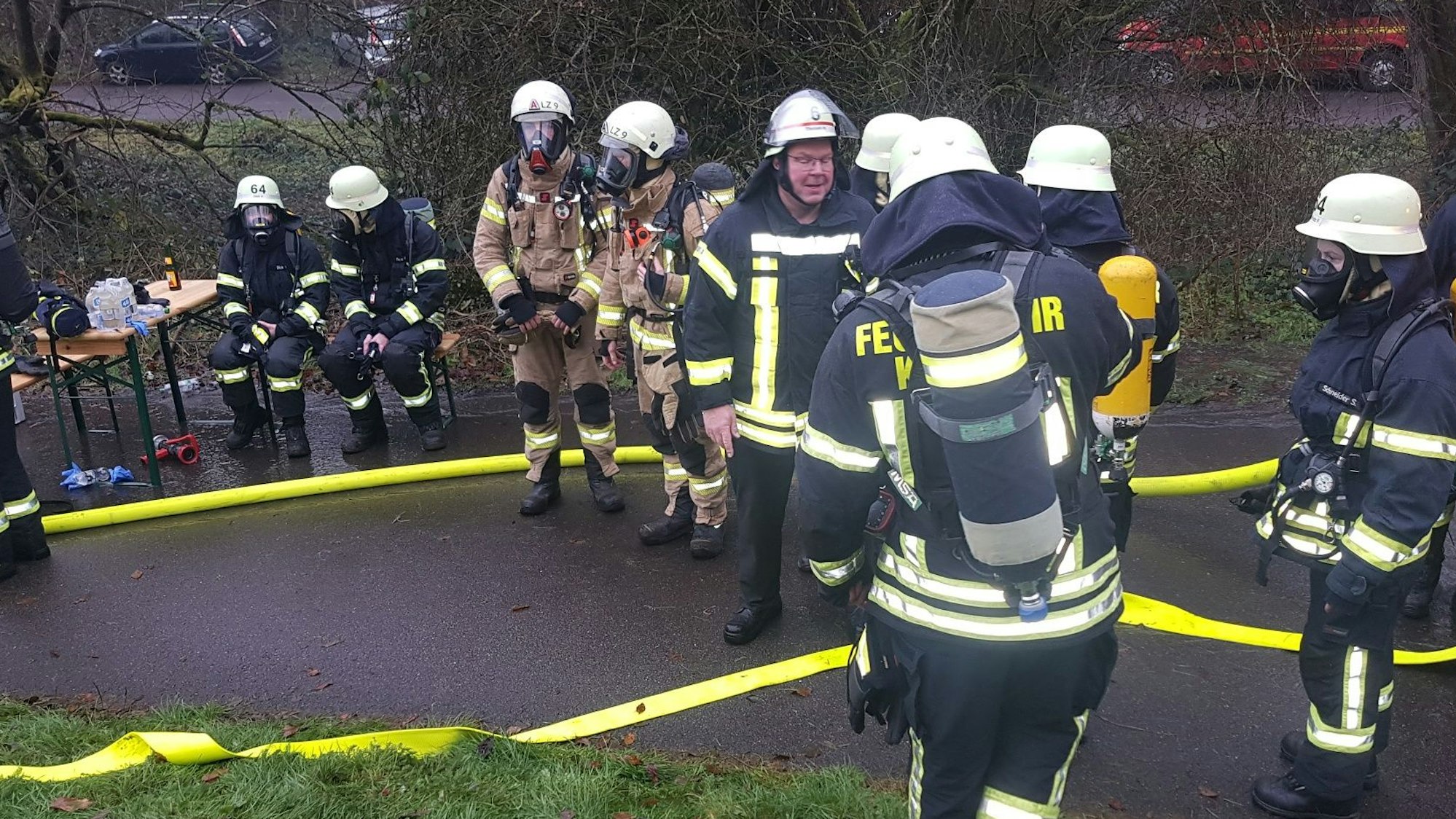 Feuerwehrleute stehen und sitzen neben einem Tisch, der auf einem Weg aufgestellt ist.