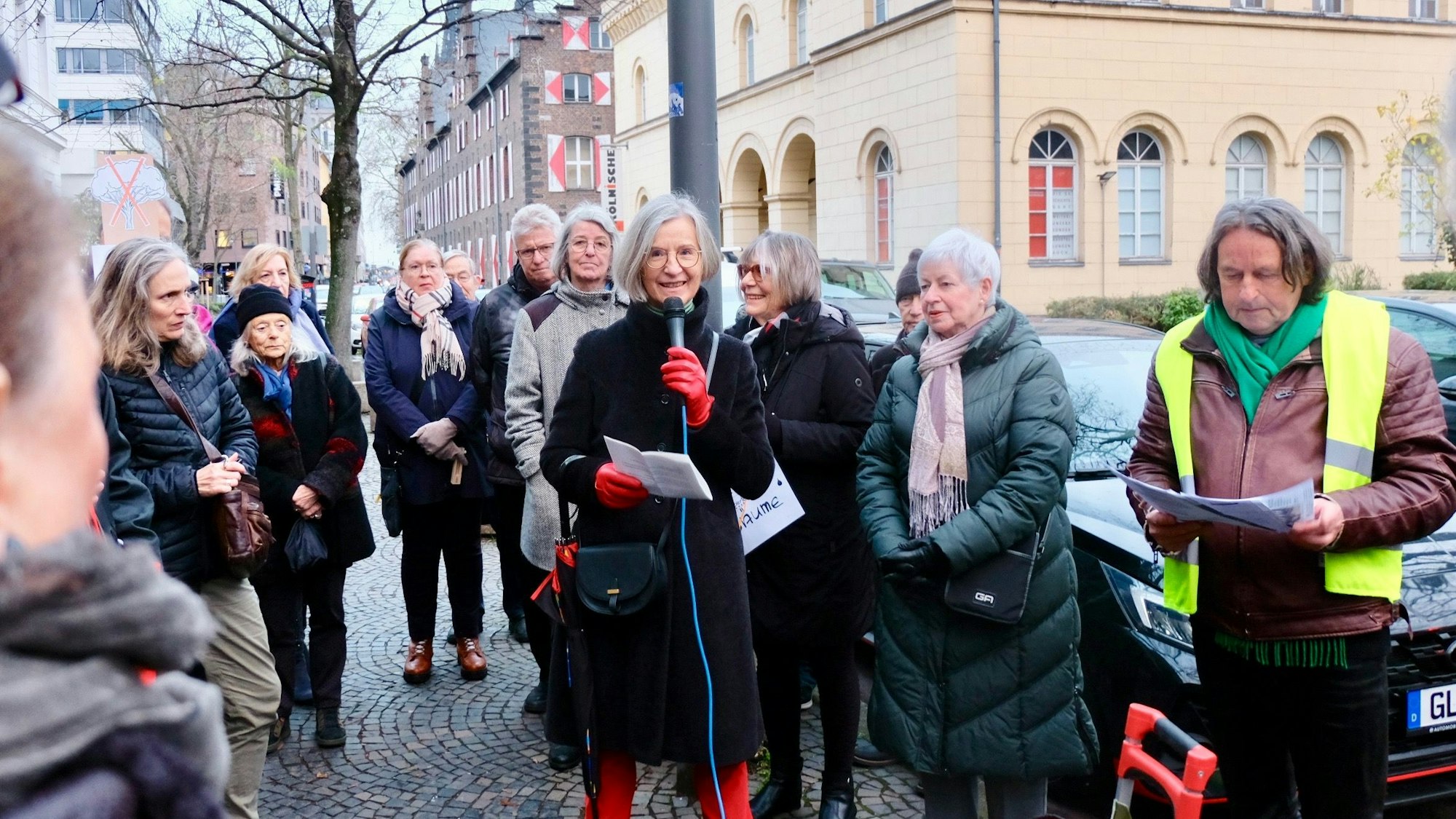 Menschen stehen zusammen auf einem Platz. In der Mitte hält eine Frau ein Mikrofon.