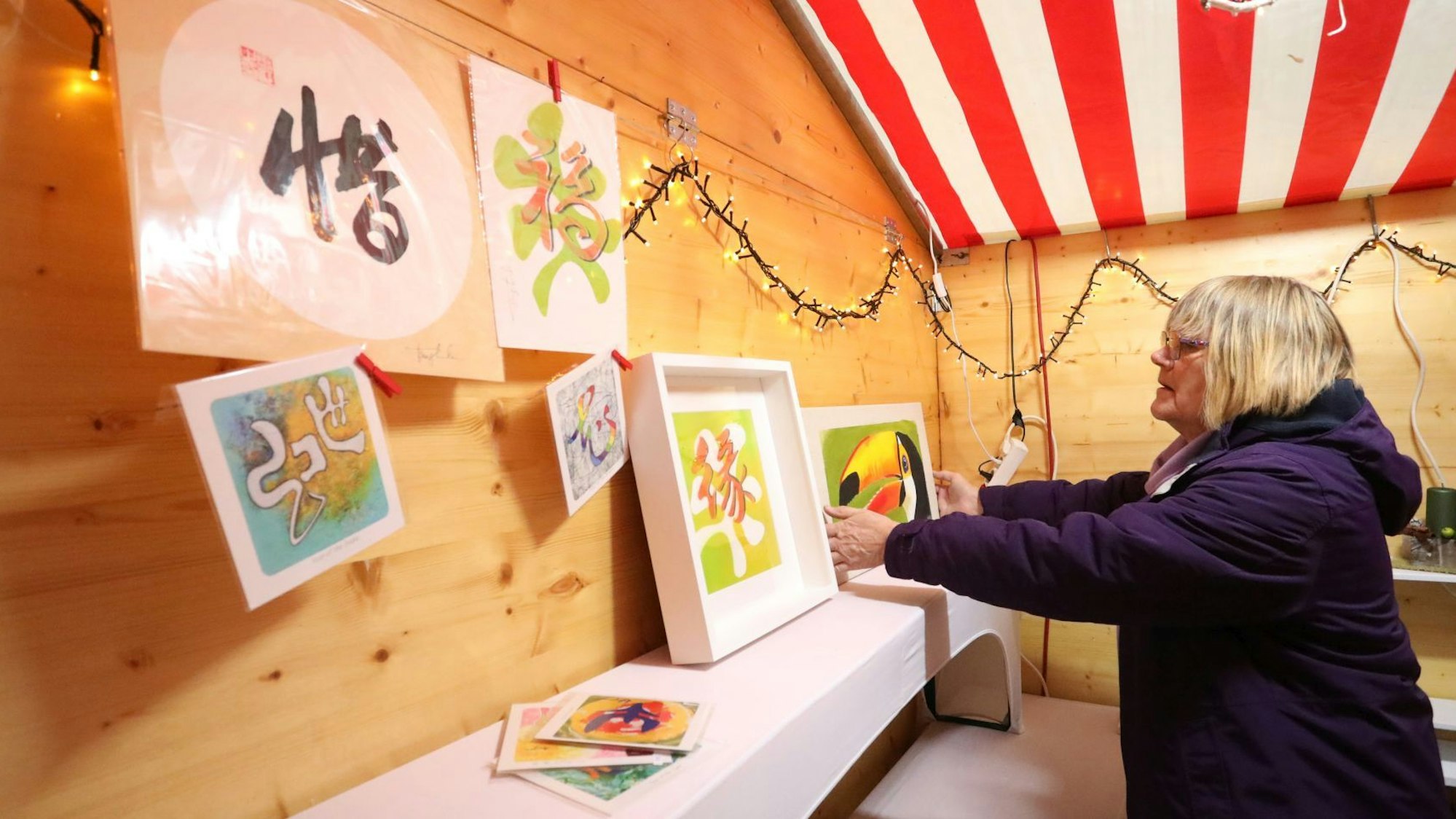 Eine Frau stellt und hängt Bilder in einer Holzbude auf.