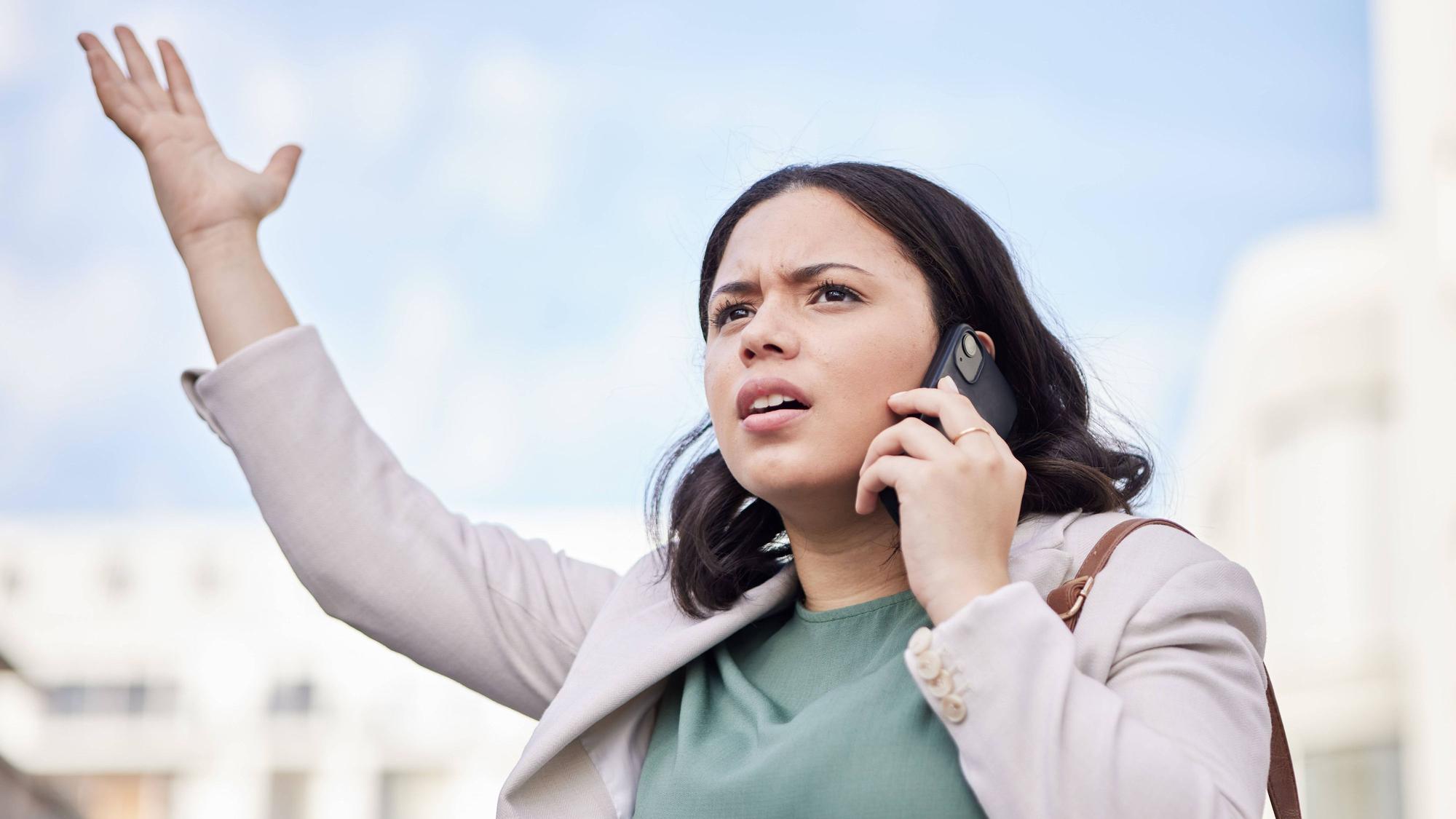 Eine Frau hält ihr Handy an ihr Ohr und blickt empört